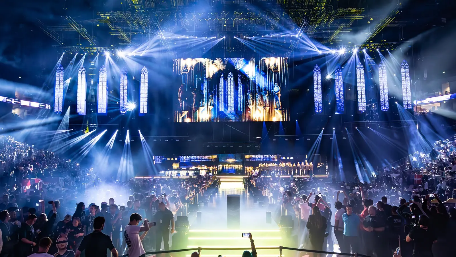 A vibrant esports LAN stage with lights and a large screen, filled with excited fans.