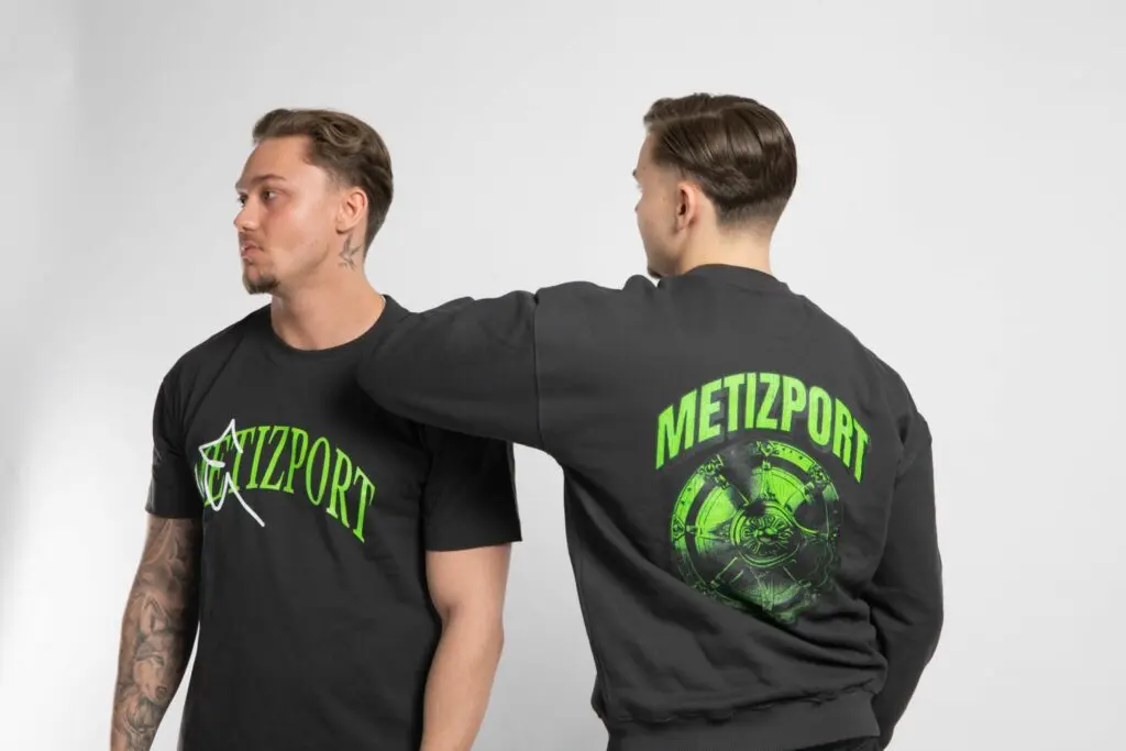 Two men wearing black Metizport team apparel, one in a t-shirt and one in a sweatshirt with green logos.