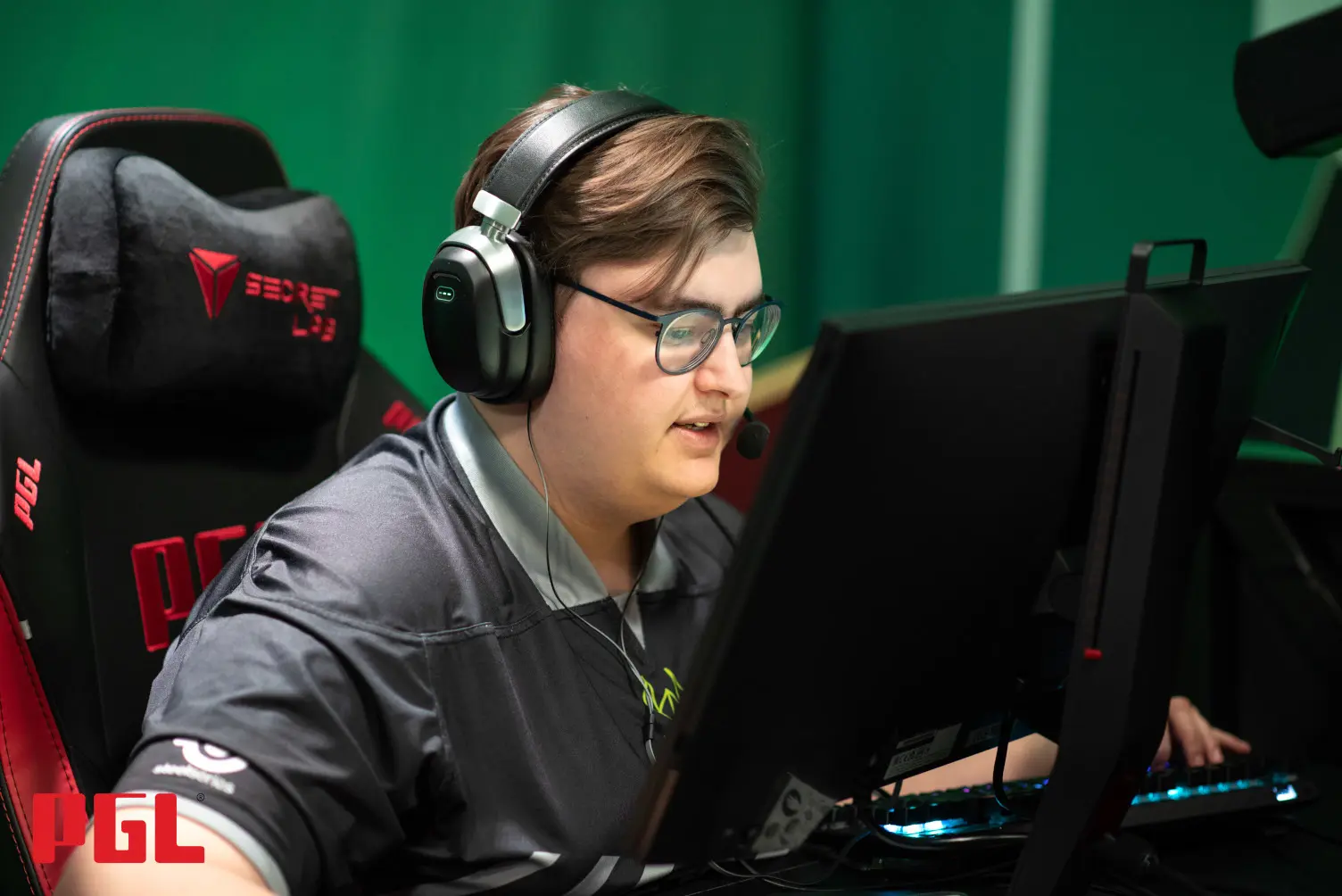 A gamer with headphones focused on a computer screen at an esports event.