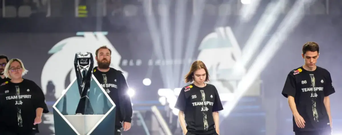 Team Spirit players wearing black team jerseys standing on a stage next to a trophy