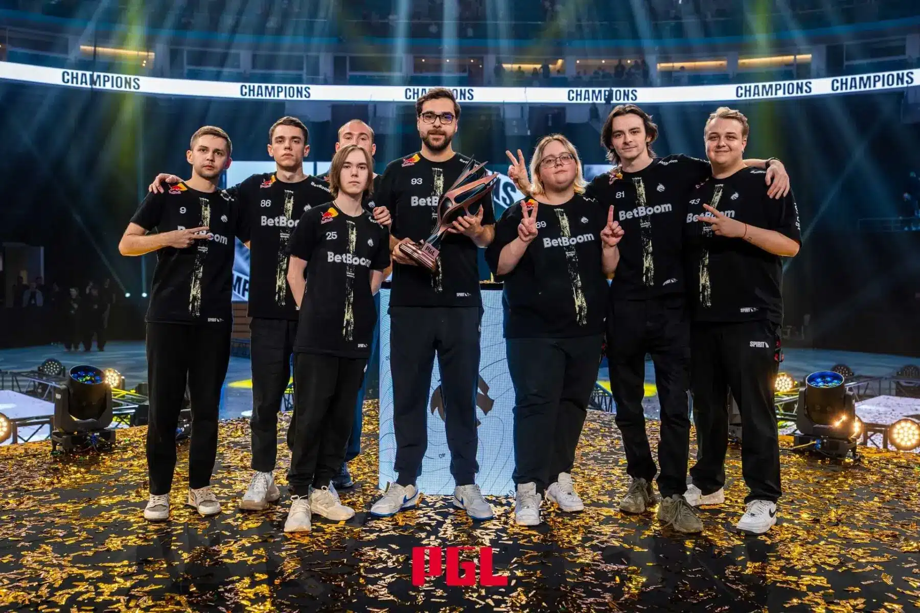 Team Spirit CS2 players posing with a trophy on a stage covered in gold confetti at a PGL tournament