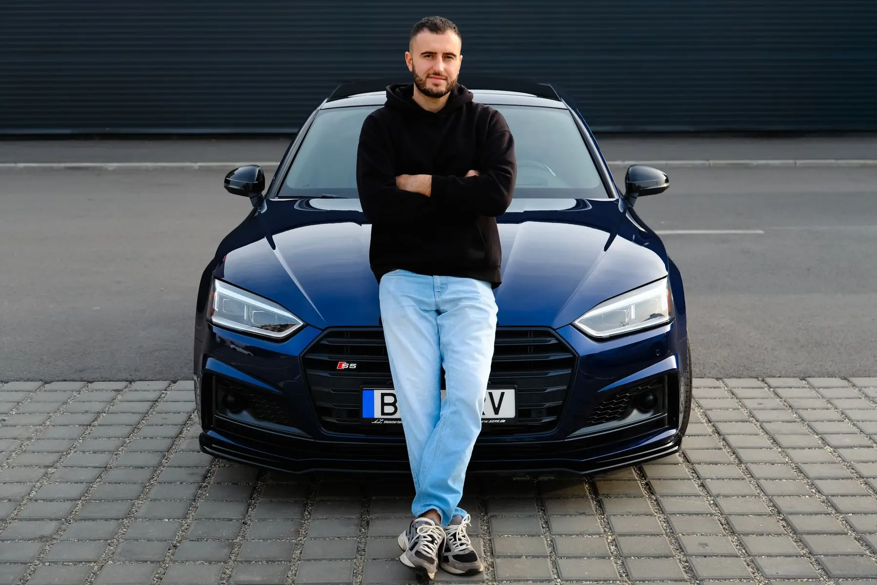 Andrey AW Anisimov standing with arms crossed in front of a dark blue Audi RS5
