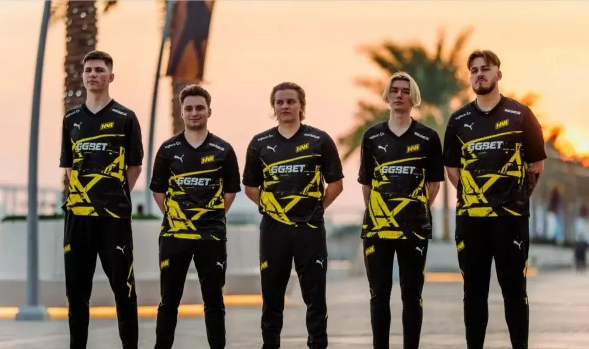 Five members of the NAVI CS2 team posing in black and yellow team jerseys against a sunset background.