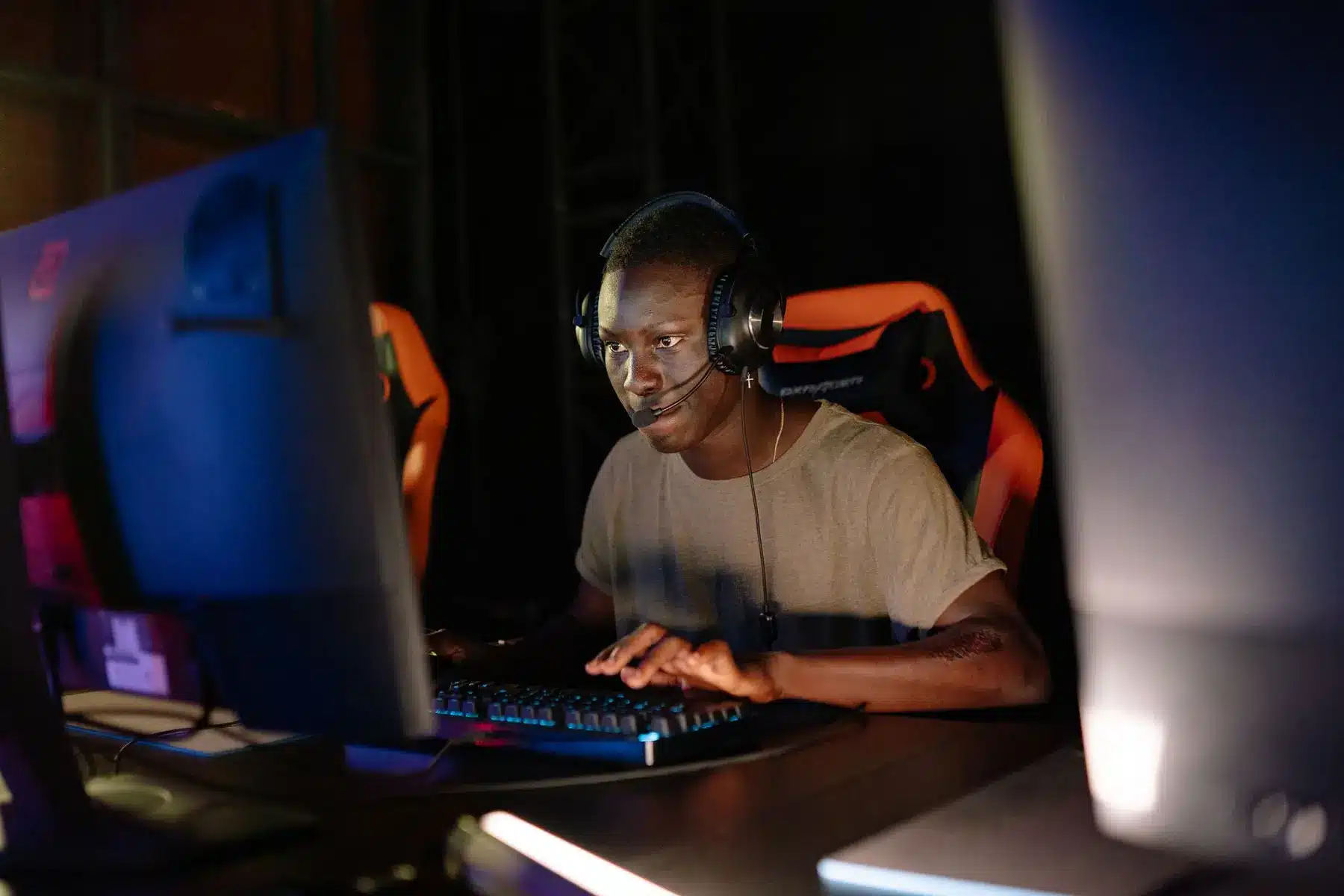A focused gamer wearing a headset and sitting in a gaming chair while playing on a computer
