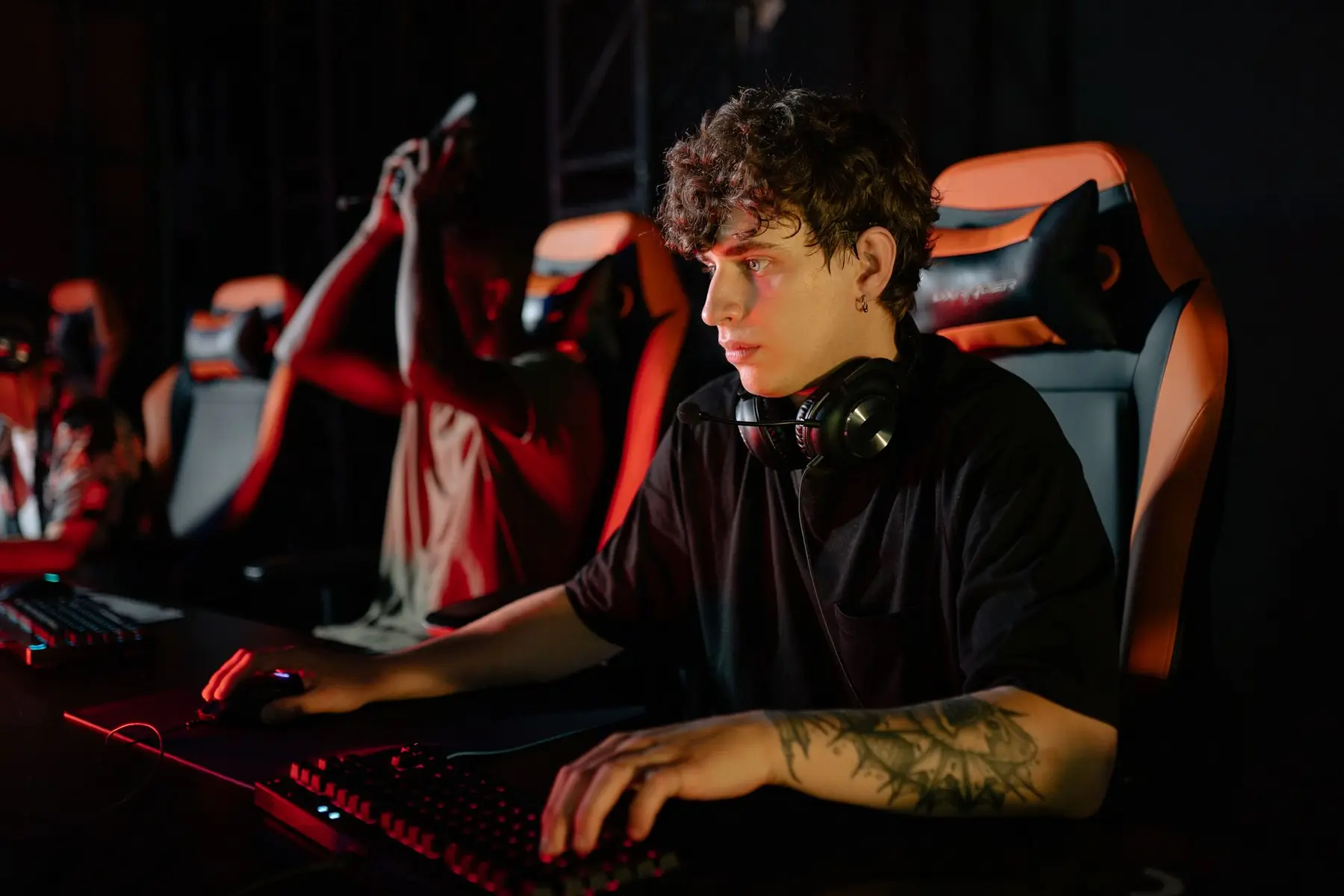 A professional gamer with tattoos and headphones focusing on a monitor with a mechanical keyboard and mouse
